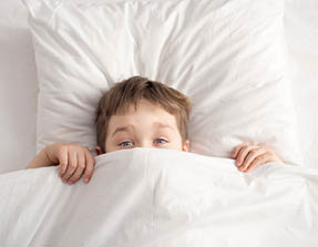 Cheerful boy in white bed under white blanket. Sleeping boy. Sleeping child