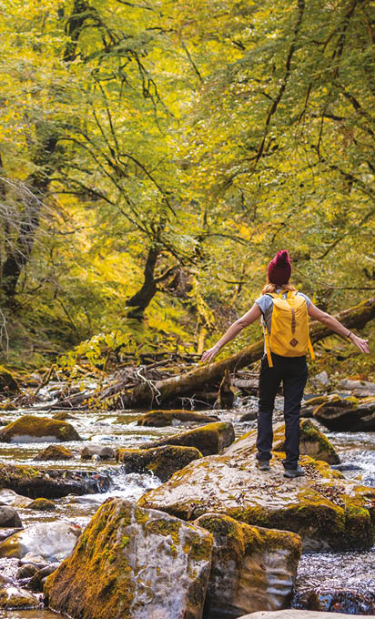 A young woman at sunset on the river on the path to the Holtzarte suspension bridge, Larrau. In the forest or jungle of Irati, Pyrenees-Atlantiques of France