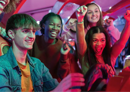 group of multiracial gamer friends playing racing arcade machines while celebrating excitedly